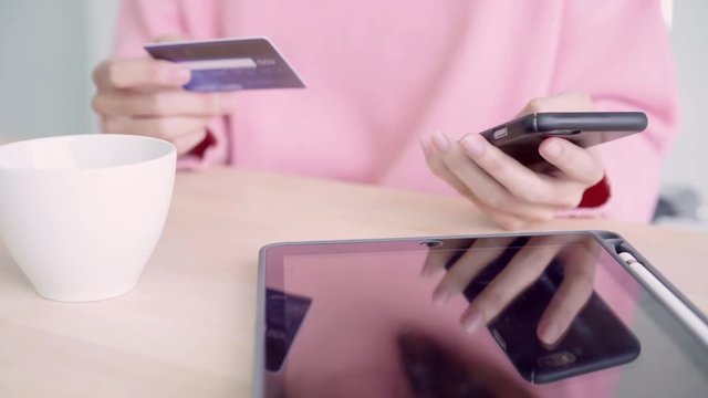 Beautiful Asian woman using smartphone buying online shopping by credit card while wear sweater sitting on desk in living room at home. Lifestyle woman at home concept.
