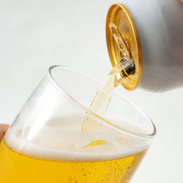 Alcoholic beverage, drinking alcohol and alcoholic content concept with close up on a hand pouring from a can of beer into a clear glass isolated on white background