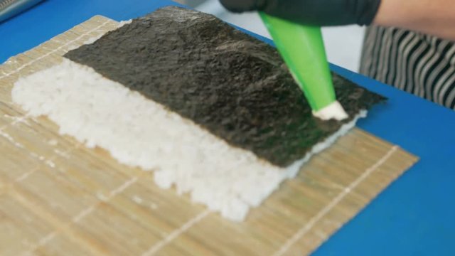 Close-up of professional chef's hands in black gloves making sushi and rolls in a restaurant kitchen. Japanese traditional food. Preparation process. step by step