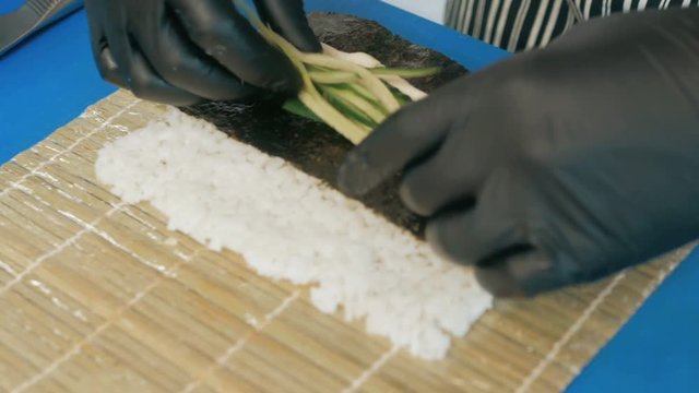 Close-up of professional chef's hands in black gloves making sushi and rolls in a restaurant kitchen. Japanese traditional food. Preparation process. step by step