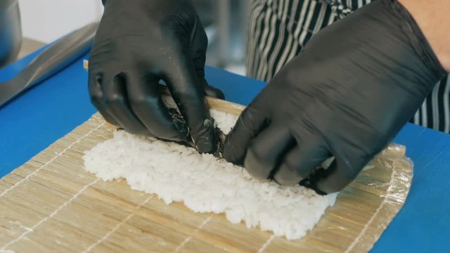 Close-up of professional chef's hands in black gloves making sushi and rolls in a restaurant kitchen. Japanese traditional food. Preparation process. step by step