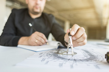 architect builder works at the table with drawings. Helmet, drawings, compasses in the workplace