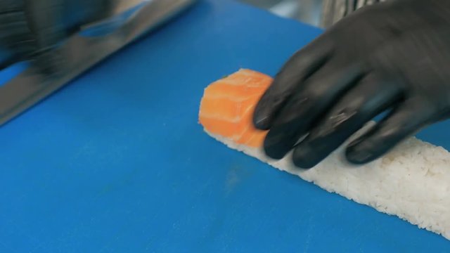 Close-up of professional chef's hands in black gloves making sushi and rolls in a restaurant kitchen. Japanese traditional food. Preparation process. step by step