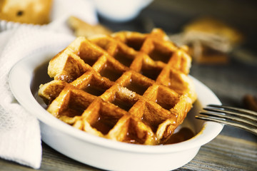 sweet waffle with condensed milk in a plate on a wooden board