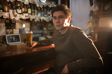 Young man drinking beer at the bar, looking in the camera