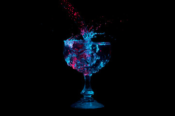 Stream of water splashing into a full glass under red and blue lights isolated on a black background