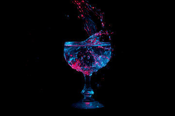 Blue and red lit clear liquid falling into and splashing in a glass goblet isolated on a black background