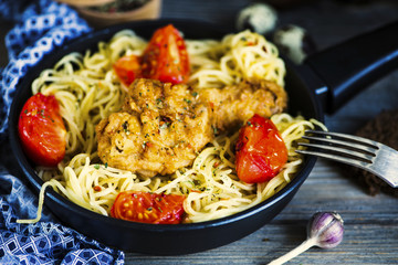 grilled chicken leg and pasta in a pan with vegetables and spices on a wooden board