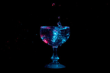 Water drops suspended in air falling into a glass chalice lit by blue and red lights isolated on a black background