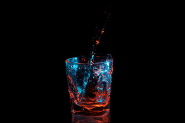 Pouring water into a rocks glass under blue and orange lights isolated on a black background
