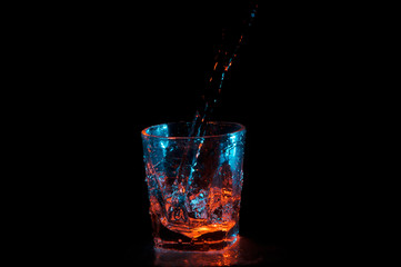 Big stream of water being poured into a square glass under blue and orange lights isolated on a black background