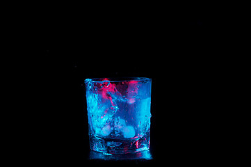 ice water in a rocks glass under colorful lights isolated on a black background
