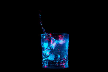 Water falling into rocks glass under colorful lights isolated on a black background