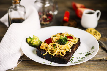 fried black bread with spaghetti and vegetables on a plate on a wooden table