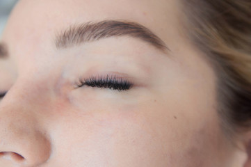 Eyelash extension procedure. Young beautiful woman eye with long false eyelashes. Close up macro shot of fashion eyes in beauty salon.