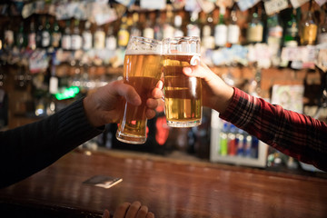 Cheers. Close-up of two men toasting with beer at the bar counter