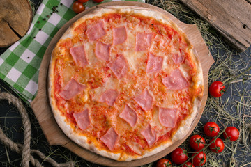 Pizza with ham on wooden background with tomatoes close up