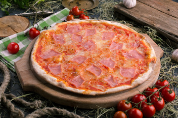 Pizza with ham on wooden background with tomatoes close up