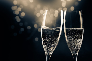 two champagne glasses ready to bring in the New Year - holiday lights and fireworks in the background