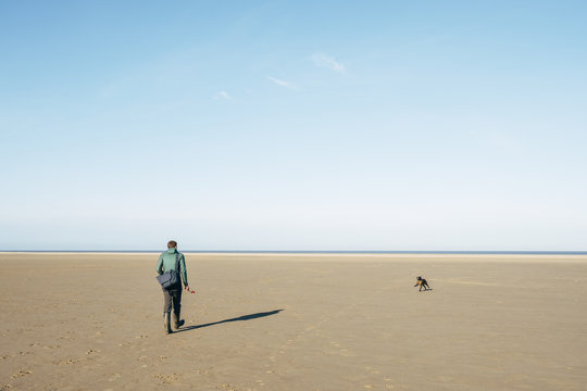 Male playing ball with his dog on a vast empty beach. Holkham, N