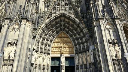 Fototapeta premium gotisches Hauptportal des Kölner Doms mit zahlreichen Statuen im seitlichen Sonnenlicht