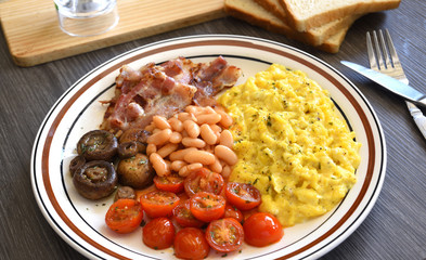 Breakfast of eggs, mushrooms, bacon, tomatoes and baked beans. 