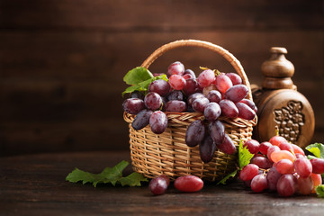 Ripe grapes in wicker basket on wooden background.