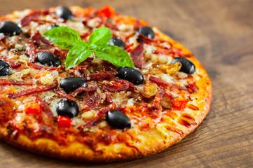 Pizza with Mozzarella cheese, salami, pepper, ham, pepperoni, olives, Spices and Fresh Basil. Italian pizza on wooden background