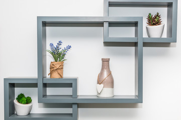 Modern decorative shelf with vases and flowers on white wall background. Close up.