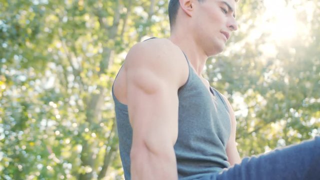 Male athlete performing difficult exercise on gymnastic parallel bars. Slim athlete a very fit guy fitness instructor or a personal trainer working out his arm muscles on outdoor beach gym as part of