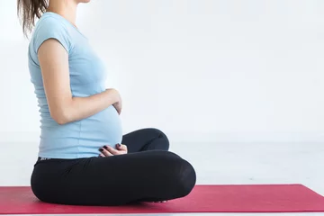 Foto auf Leinwand pregnancy, sport, fitness, people and healthy lifestyle concept - happy pregnant woman exercising yoga and and meditating in lotus pose in white background gym © xartproduction