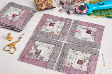 Patchwork log cabin blocks, stack of blocks, sewing accessories on white wooden surface