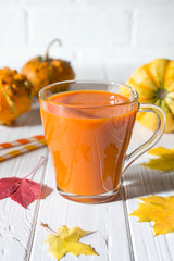 Fresh pumpkin juice in glass cup, pumpkins and fallen maple leaves. Fall drink concept