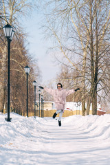 Cheerful Young stylish woman jumping in the air in the park on a sunny winter day. Winter fun.