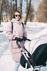 Young mother wlalking with a newborn child in the park in winter. Sunny winter day walk.