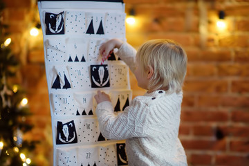 Happy little boy takes sweet from advent calendar on Christmas eve