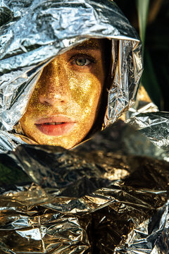 Portrait of woman with golden face and covered by silver material
