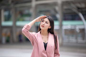Young Asian woman wear pink suit   holding dollars against blurred city background very happy pointing with hand and finger to the side