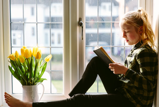 Pre-teen girl sitting in a sunny window reading