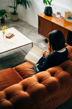 Girl reading on a orange velvet chester sofa