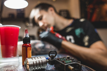 The tattoo artist creates a picture on the body of a man. close-up of tattoo machines and paints