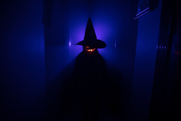 Halloween concept. Creepy silhouette in the dark corridor with pumpkin head. Toned light with fog on background. Selective focus
