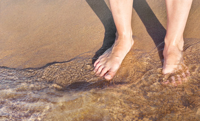 Women's feet are in water at the sea beach.