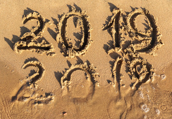 New year 2019 concept. Inscription 2018 and 2019 on a beach sand, sea wave covering digits 2018.