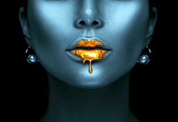 Goldfarbe tropft von den sexy Lippen, goldene Flüssigkeitstropfen auf den Mund des schönen Modellmädchens, kreatives abstraktes dunkelblaues Hautmake-up. Gesicht der Schönheitsfrau © Subbotina Anna