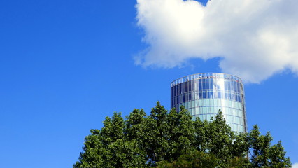 Obraz premium Aussichtsturm Triangle in Köln ragt über die Bäume in den blauen Himmel mit weißen Wolken