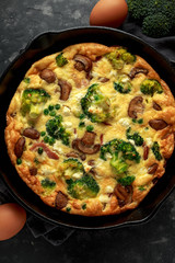 Homemade Frittata with mushrooms, broccoli, feta cheese, green peas and bacon on cast iron skillet