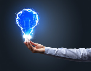 Hand holding shiny light bulb on dark background. New idea concept