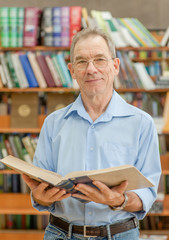 senior man with open book in the library looking at camera