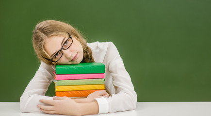Teen girl hugs a stack of books on the background of a school board. Space for text